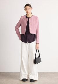 Jachetă scurtă, roz deschis, cu guler rotund și patru nasturi aurii, asortată cu o cămașă mov închis și pantaloni albi largi. Poșetă și pantofi negri.