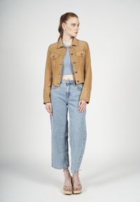 Tan leren jack met knoopsluiting en twee voorkanten zakken, gecombineerd met een lichtblauw cropped gestreept top en wijde denim jeans.