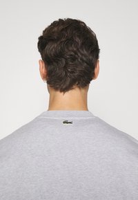 Felpa grigia in misto cotone, con scollatura rotonda e logo di un coccodrillo ricamato sulla parte superiore della schiena. Finitura testurizzata.