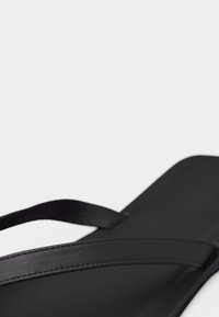 Κοντινό πλάνο ενός μαύρου σανδάλιου τύπου σαγιονάρας με λεπτές λουρίδες και επίπεδη σόλα σε λευκό φόντο.