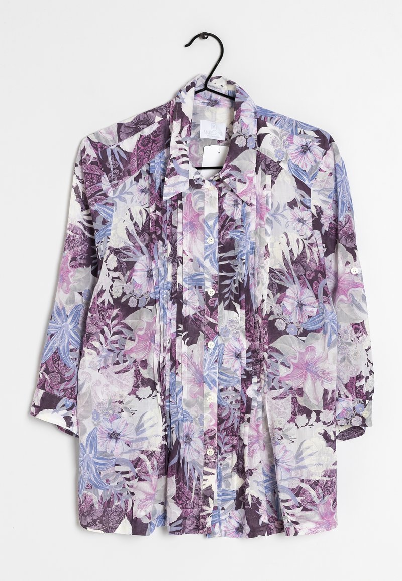 Chemise à manches longues boutonnée avec imprimé floral et feuilles violet, rose et bleu, suspendue sur un cintre noir sur fond blanc.