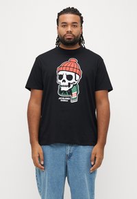 Μαύρο βαμβακερό t-shirt με πολύχρωμο γραφικό ενός κρανίου που φοράει κόκκινο σκουφάκι, με πράσινες και λευκές λεπτομέρειες στο μπροστινό μέρος.