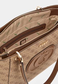 Borse a mano marrone con motivo e accessori in oro, dotata di un logo testurizzato, numerosi scomparti interni e una fodera beige con branding ripetuto.