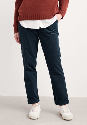 Donkerblauwe, op maat gemaakte broek van zachte stof, met een rechte pasvorm en opgerolde manchetten, gecombineerd met een witte overhemd en lichte sneakers.