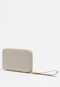 Billetera de color gris claro con un acabado de cuero suave, forma rectangular, cremallera dorada y correa para la muñeca. Sin patrones ni hardware adicional visible.