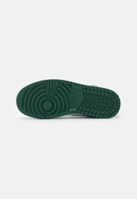 Semelle d'une basket Nike vert foncé avec des motifs de marche circulaires et en quadrillage sur fond blanc.
