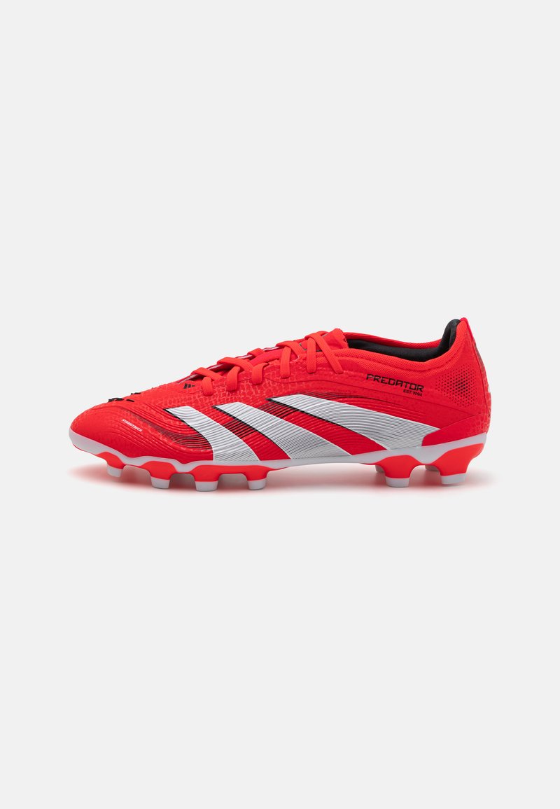 Rote und silberne Fußballschuhe mit einer strukturierten Oberseite, Schnürdesign und geformten Stollen an der Sohle für Griffigkeit. Auffällige "Predator"-Markierung.