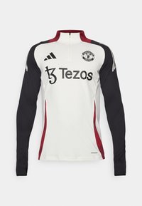 White long-sleeve training top with black sleeves, a quarter zip collar, red accents, Manchester United logo, and Tezos branding on the front.
