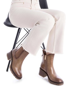 Botas de tobillo marrones con un acabado brillante, inserts laterales elásticos y un detalle de cremallera. Tacón grueso y suela texturizada, combinadas con jeans de tono claro.