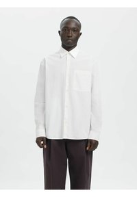 Weißes Langarmhemd mit vertikalen Streifen, mit Knopfkragen, einer Brusttasche, kombiniert mit dunklen, locker sitzenden Hosen.