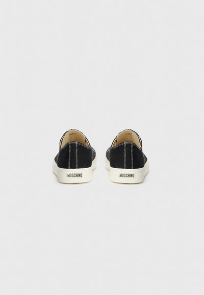 Svarta mockaskor i slip-on stil med vit sömnad och vit gummisula. "Moschino"-logotyp på klacken. Platt design med rund tå.