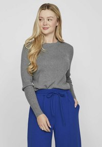 Suéter gris con acanalados y mangas largas, combinado con pantalones azul con cuerda ajustable. El atuendo presenta una silueta ajustada y una textura suave.
