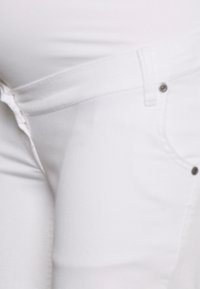 Jeans de ganga branca com um estilo clássico de cinco bolsos, com fecho de zip e detalhes em botão prateado. Textura suave e design ajustado.