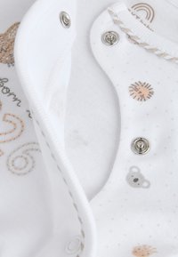 Vita babykläder med tryckknappar, med små beige och grå djur- och naturmotiv, inklusive en koala och en sol.