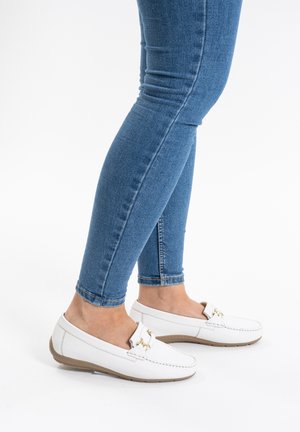 White leather loafers with a round toe, accented by gold hardware, paired with blue skinny jeans. Textured upper and flexible sole.