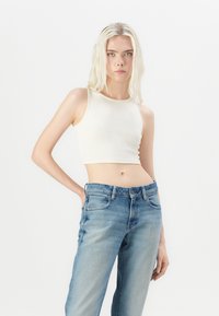 Top scurt ribbed de culoare albă murdară, cu decolteu rotund, asortat cu blugi drepti de culoare albastru-medie, având design clasic cu cinci buzunare.