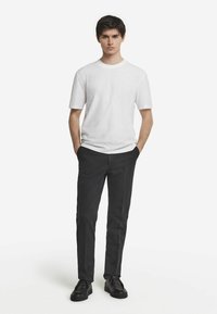 Hvid kortærmet t-shirt parret med sorte bukser, der har lige snit og lommer. Modellen bærer sorte sko for et fuldendt look.