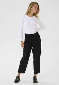 Haut à manches longues blanc à côtes avec un col henley et cinq boutons, associé à un pantalon noir plissé taille haute et des mocassins noirs épais.