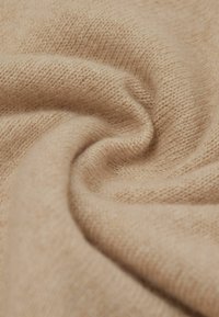 Lys beige strikket stof med en blød, tekstureret overflade, der har en glat fald og subtile, fine fibre, der er vævet ind i det.