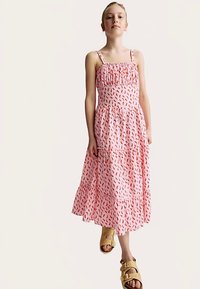 Abito midi rosa con motivo di foglie astratte rosse, balze a ruota e sottili spalline regolabili. Indossato con sandali color cuoio.