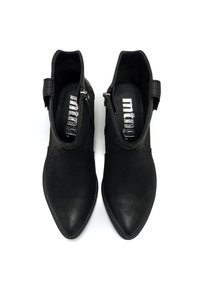 Une paire de bottines en cuir noir avec des pointes effilées et des zips sur les côtés, vues d'en haut sur un fond blanc.