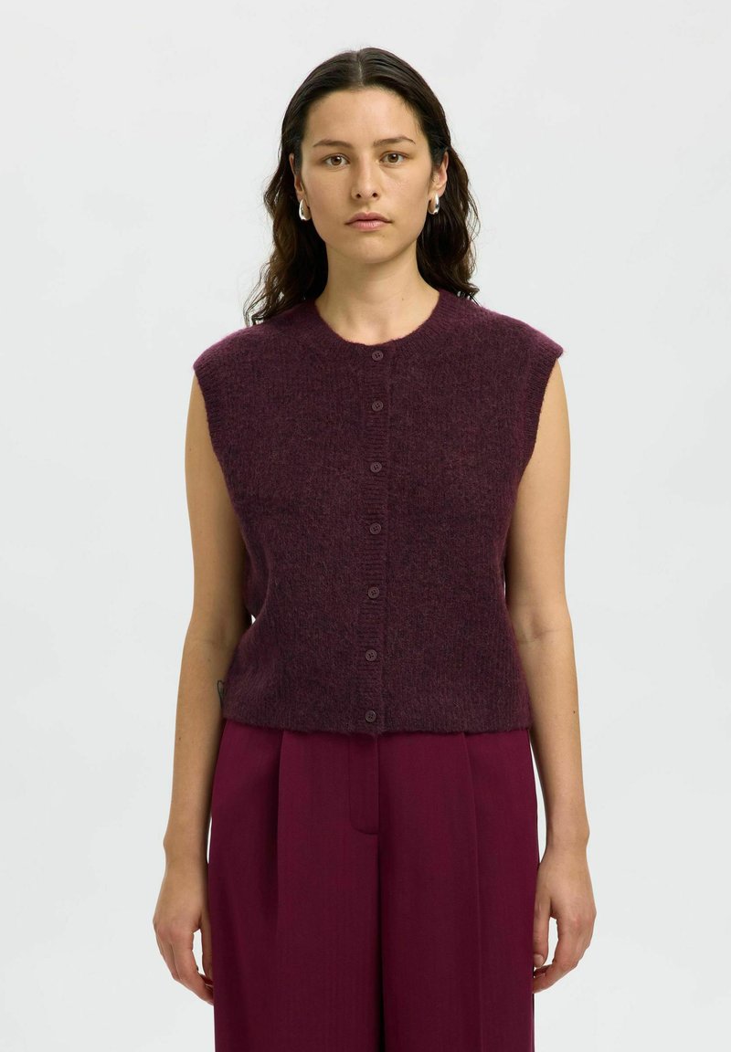 Gilet senza maniche di un profondo borgogna, lavorato a maglia, con scollatura rotonda, bottoni frontali e una texture morbida, abbinato a pantaloni a vita alta coordinati.