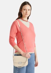 Pull en corail à col en V avec des manches longues, superposé sur un haut clair, associé à un sac bandoulière crème doté d'un fermoir en argent et d'une bandoulière en chaîne.