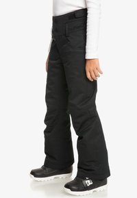 Schwarze Schneehosen mit geradem Design, ausgestattet mit zwei Knöpfen, einem Klettverschluss und verstärkten Nähten; kombiniert mit schwarzen Stiefeln.
