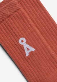 Roestkleurige geribbelde sokken met witte geborduurde letter "A". Zacht materiaal met een gestructureerde afwerking.