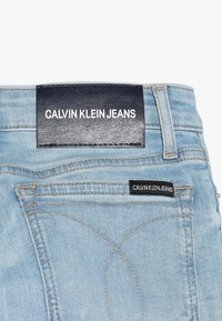 Ljusblå denimjeans med en svart läderlapp som säger "CALVIN KLEIN JEANS" vid midjan och en liten svart etikett på fickan.