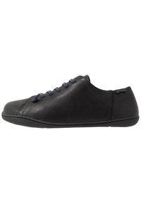 Zapato de cuero negro con un perfil bajo, punta redonda y cordones azul marino. Presenta una textura suave y detalles de costura a lo largo de los lados.