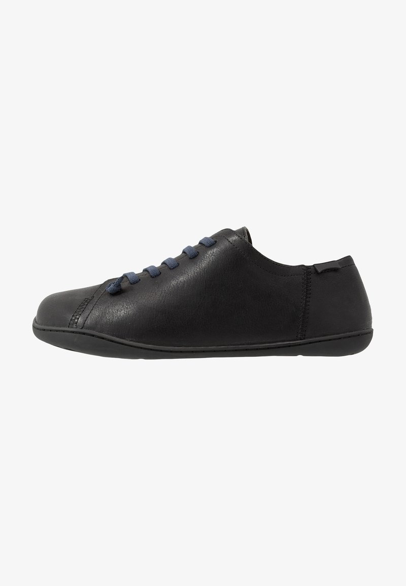 Zapato de cuero negro con un perfil bajo, punta redonda y cordones azul marino. Presenta una textura suave y detalles de costura a lo largo de los lados.
