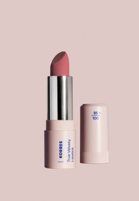 KORRES Prawdziwa Aksamitna Pomadka, jasnoróżowa cylindryczna tubka, srebrny metalowy szpic, z niebieskim napisem, gładka tekstura, wraz z nakrętką.