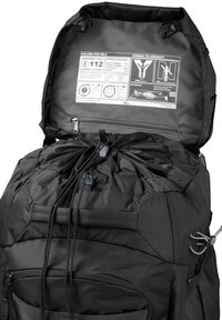 Mochila negra con exterior texturizado, cierre por cordón, múltiples cremalleras y etiquetas de información de emergencia en el interior de la solapa superior.