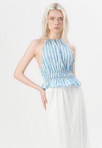 Top halter a rayas en azul claro y blanco, con cintura fruncida y detalle de peplum, combinado con una falda blanca de encaje que presenta patrones intrincados.