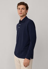 Granatowa koszula polo z długim rękawem wykonana z bawełny, z klasycznym kołnierzykiem, trzema guzikami oraz prostym dołem. Minimalistyczny design.