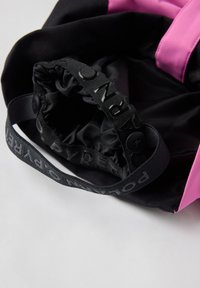 Mustaksi värjätty kangaskassi, jossa on vaaleanpunaisia yksityiskohtia. Kassi on varustettu kerrotulla ylhäisellä osalla ja mustalla hihnalla, jossa on kohollaan olevaa tekstiä. Kassi on sileä tekstuuriltaan ja sen muotoilu on yksinkertainen.