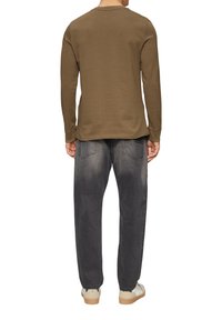 Camicia in cotone marrone a maniche lunghe con scollatura rotonda, abbinata a jeans denim grigi strappati e sneakers di colore chiaro.