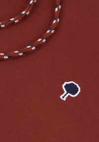 Rustkleurige stof met een gestructureerde afwerking, voorzien van een blauw geborduurd logo met witte rand en een gevlochten meerkleurig koorddetail.