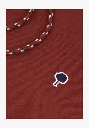 Rustkleurige stof met een gestructureerde afwerking, voorzien van een blauw geborduurd logo met witte rand en een gevlochten meerkleurig koorddetail.