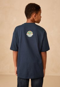 Navy blue cotton T-shirt with short sleeves and a round neckline; features a graphic design on the back depicting a character and circular emblem.