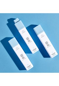 Three white and light blue bottles of Drunk Elephant B-Hydra Intensive Hydration Serum on a blue background.