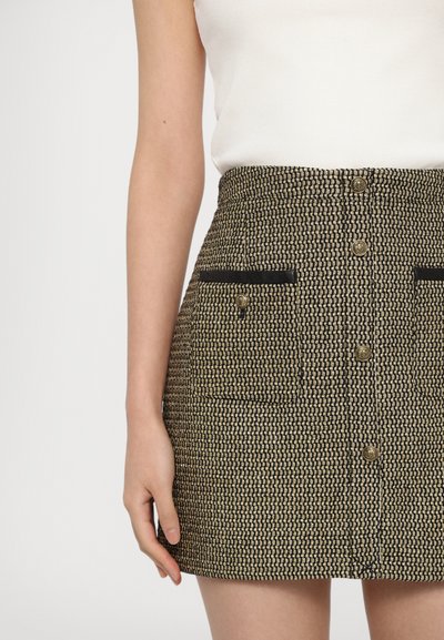 A fitted skirt in a textured woven fabric, featuring a black and gold pattern, two front pockets, and gold button accents.