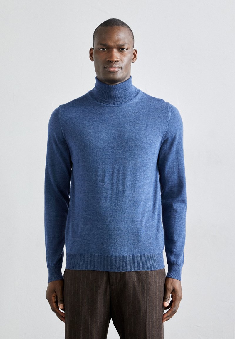 Blå turtleneck genser laget av mykt stoff, med lange ermer og ribbede mansjetter, akkompagnert av brune stripete bukser.