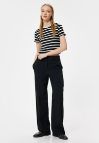 Camisa de rayas blanca y negra, de mangas cortas, combinada con pantalones negros de cintura alta. Textura suave, diseño minimalista, corte relajado.