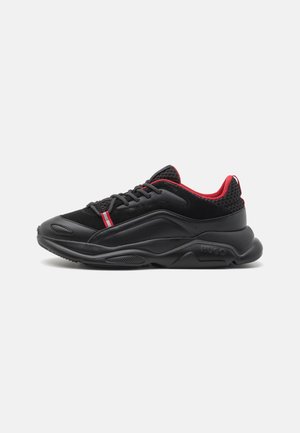 Sort og rød lavtop sneaker med tyk sål, struktureret overdel, sorte snørebånd, rød inderforing og lille rød og hvid flap nær snørebåndene.