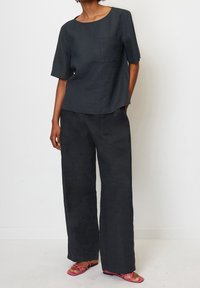 Tmavě šedý lněný top s krátkými rukávy a náprsní kapsou, doplněný širokými lněnými kalhotami. Nošené s růžovými sandály na plochém podpatku.