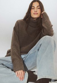 Bruine turtleneck trui van een zachte stof met ribbeldetails. In combinatie met lichtblauwe wijde jeans en zwarte enkellaarsjes.