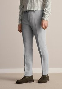 Lys grå linnedragt med en lige, skræddersyet pasform. Bæres med en olivengrøn slip-on sko og en stribet skjorte med knap.