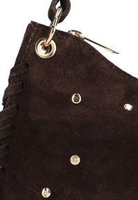 Bruin suède materiaal met complexe veters aan één zijde, gouden hardware accenten en decoratieve ronde studs over het oppervlak.